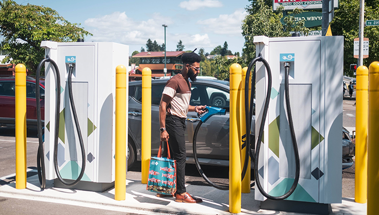 一名男子一手拎着购物袋，一手拿着电动汽车充电嘴, 他在电动汽车充电站给自己的车充电后
